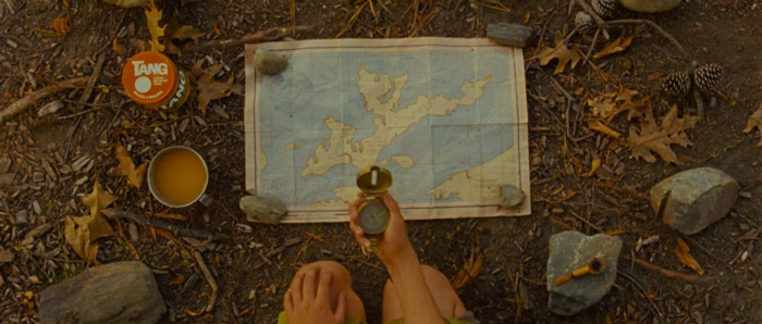 O escoteiro Sam Shakusky examina um mapa cuidadosamente arrumado no chão da floresta em "Moonrise Kingdom", de Wes Anderson.